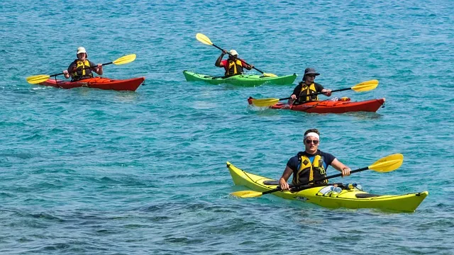 Gemeinsam paddeln – Kanu & Kajak als Gruppen-Erlebnis Vier Personen paddeln in bunten Kajaks durch türkisfarbenes Meer – Gruppenaktivität für Rafting – Paddelsport im Urlaub